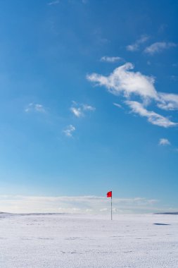 Snow covered deserted golf green with red flag, on Cleeve Hill,  clipart