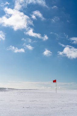 Snow covered deserted golf green with red flag, on Cleeve Hill,  clipart