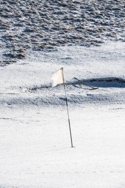 Snow covered deserted golf green with white flag, on Cleeve Hill clipart