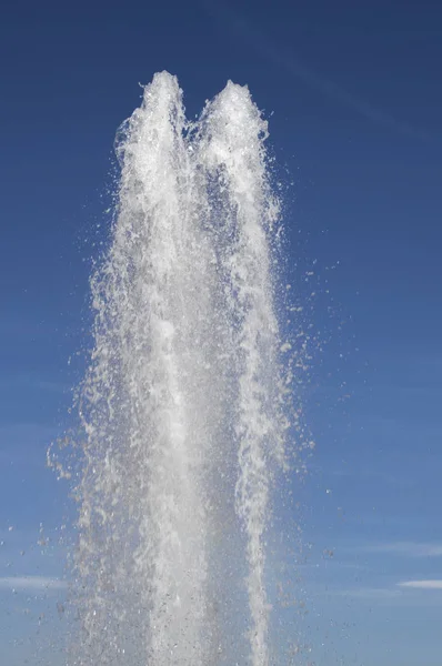 Water jet from a vertical fountain cut out against a blue sky.