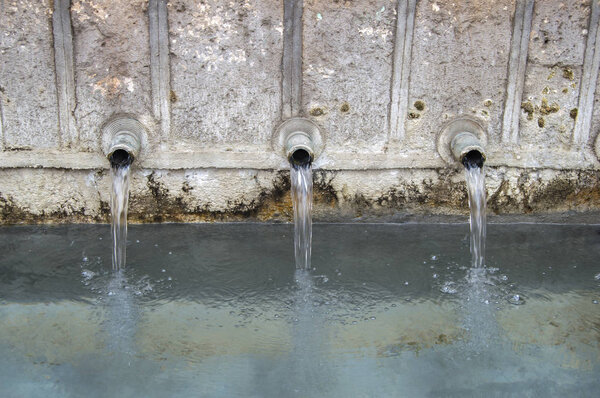 water falling from three pipes of a stone fountain. viewed closely