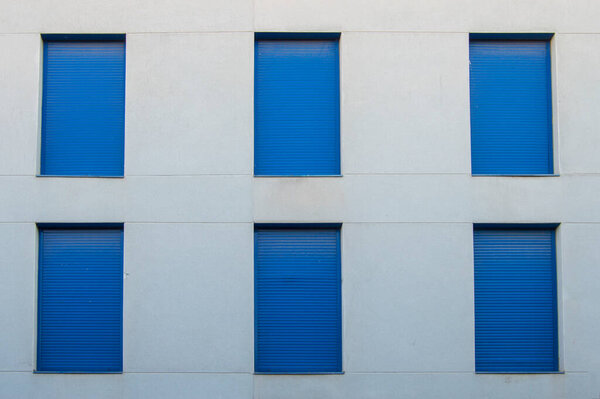 Building facade with six vertical windows closed with blue shutters
