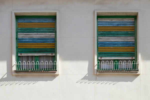Dwa Równe Okna Białej Fasadzie Niebieskimi Żółtymi Zielonymi Białymi Okiennicami — Zdjęcie stockowe