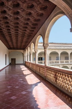 Gallery with semicircular arches, columns, and wooden ceiling panels in the Santa Cruz Museum in Toledo, Spain.