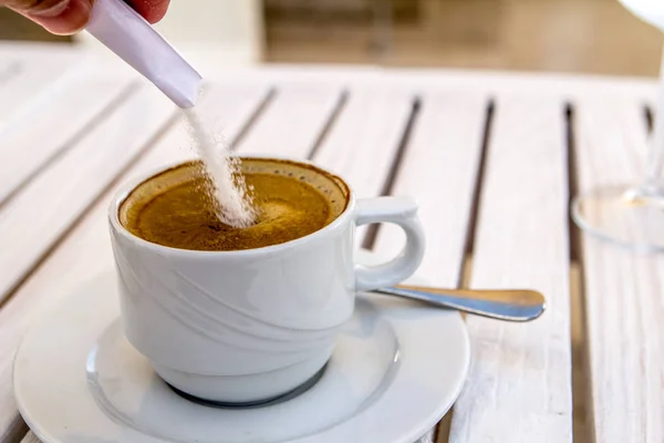 Bir güneşli yaz gününde beyaz ahşap bir masa üzerinde bir kapuçino cup şeker ekleme