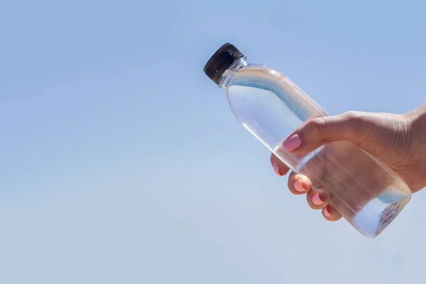 Butelka z wodą w dłoni na tle morza — Zdjęcie stockowe