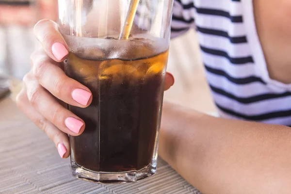 Pembe manikür ile güzel kız tutar ve güneşli sıcak bir günde buz parçaları ve bir saman ile soda ile büyük bir bardak içme.