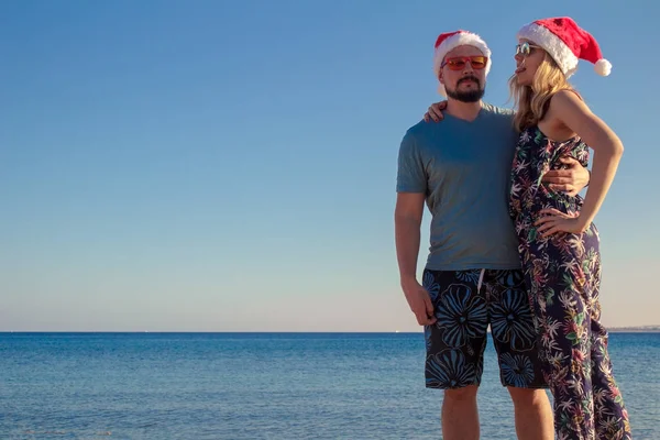 Homme et femme embrassant dans des chapeaux de Noël et des lunettes de soleil à la plage de la mer — Photo