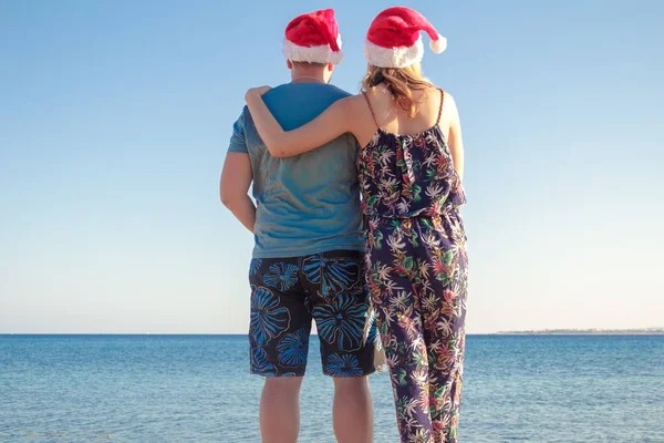 Homme étreignant femme dans des chapeaux de Noël et regardant la plage de la mer — Photo