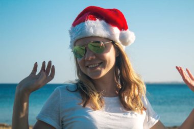 Santa Claus şapka ve güneş gözlüğü güneşli bir plaj oldukça genç bir kadın portresi. Tonda.