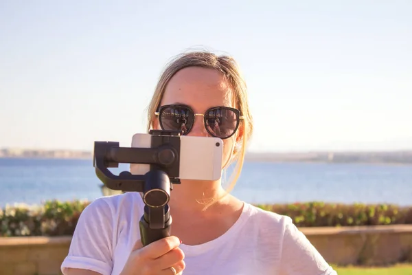 Woman filming sunset on travel, video blogger making video with gimbal and mobile phone, sunset seaside scene