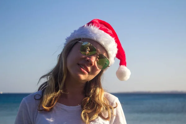 Portret van een mooie jonge vrouw in Kerstman hoed en zonnebril op een zonnig strand. Toned. — Stockfoto