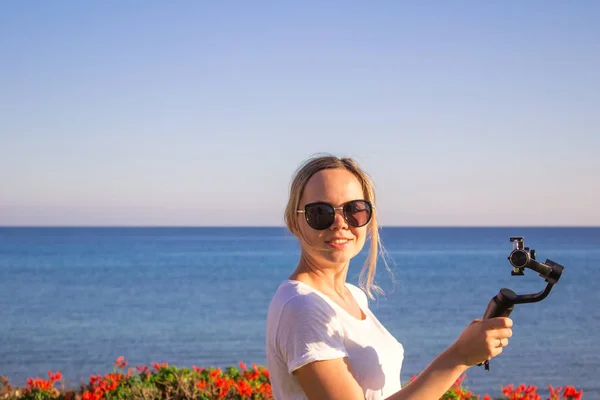 Woman filming sunset on travel, video blogger making video with gimbal and mobile phone, sunset seaside scene