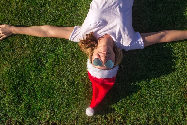 Portrait d'une jolie jeune femme en chapeau de Père Noël et lunettes de soleil sur herbe verte. tonique . — Photo