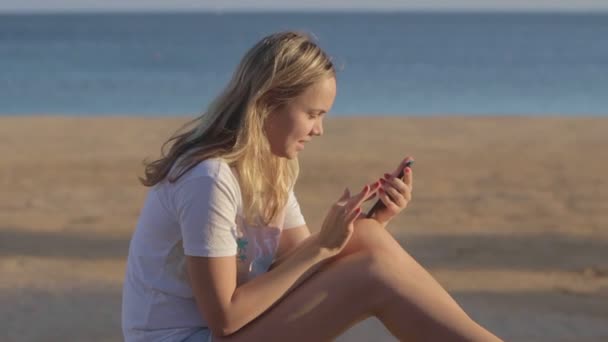 Chica con teléfono móvil en la playa en el viaje de verano en el mar — Vídeos de Stock