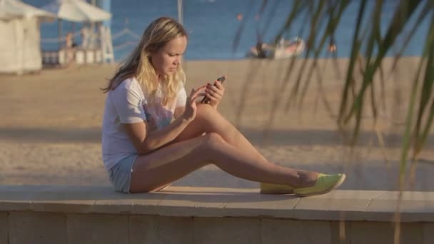 Chica con teléfono móvil en la playa en el viaje de verano en el mar — Vídeo de stock