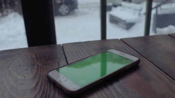 Man handen typen op groen scherm mobiele telefoon op houten tafel in café. — Stockvideo