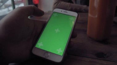 Adam yeşil ekran cep telefonu kafede ahşap masa üzerinde yazarak eller.