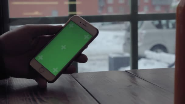 Мужские руки, печатающие на зеленом экране мобильного телефона на деревянном столе в кафе . — стоковое видео