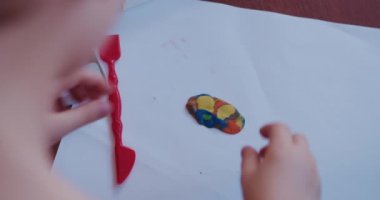 Küçük bir çocuk masada oturan parlak kil ya da plastikle oynar..