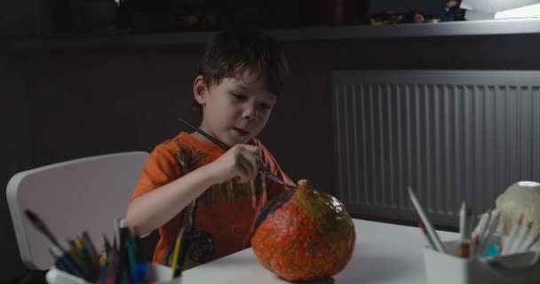Cadılar bayramı için balkabağı süsleyen ve boyayan bir çocuk. — Stok video