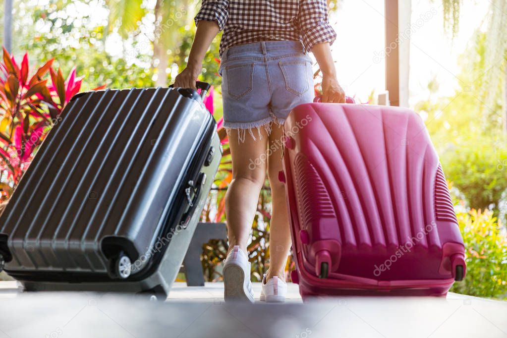 Woman with suitcase walking away. Woman walking away back view in a denim shorts and sneakers. Suitcases.