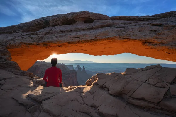 Člověk sedí na okraji a dívá se na Mesa arch východ slunce — Stock fotografie