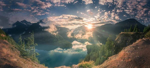 Blick Auf Strahlenden Sonnenuntergang Und Nebelschwaden Über See Und Berge lizenzfreie Stockfotos