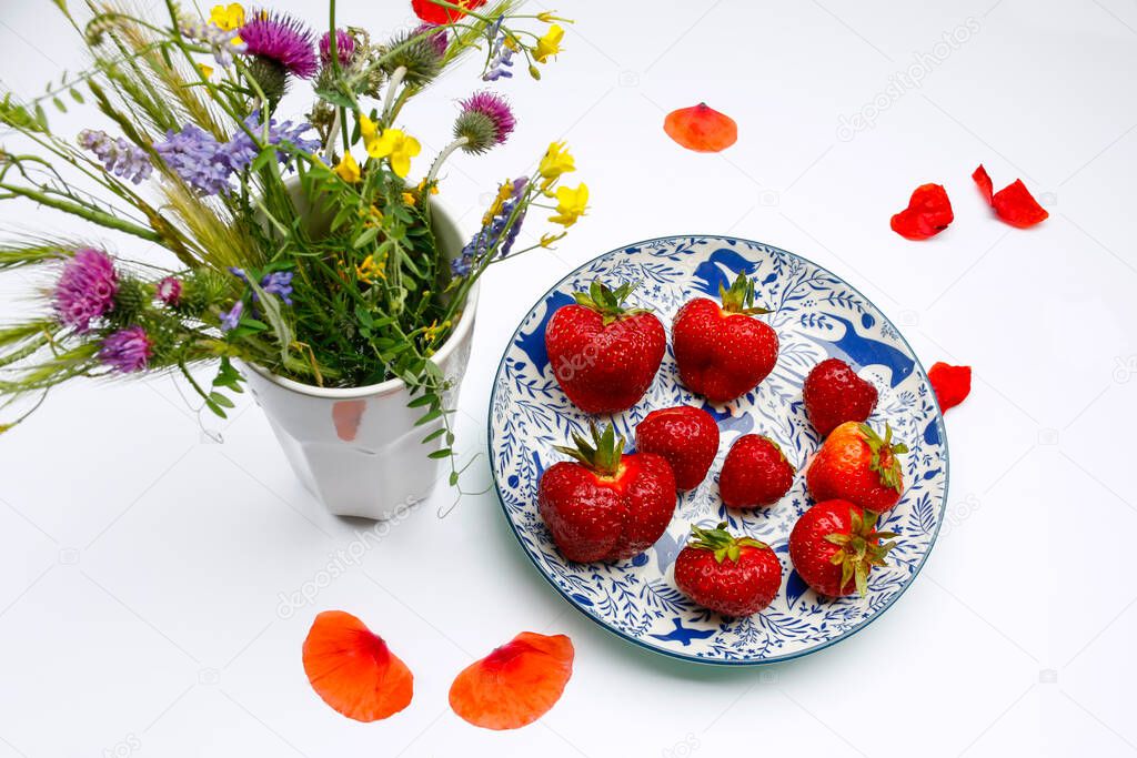 summer composition, bouquet of field flowers and juicy strawberries