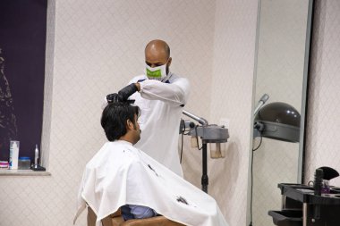 Jodhpur, Rajasthan, Hindistan, 24 Nisan 2020: Bir müşteriye saç kesen maske takan, eldiven takan profesyonel bir kuaför, salon ve berber dükkanının kilit altında tutulduktan sonra tekrar açılmasına izin verildi