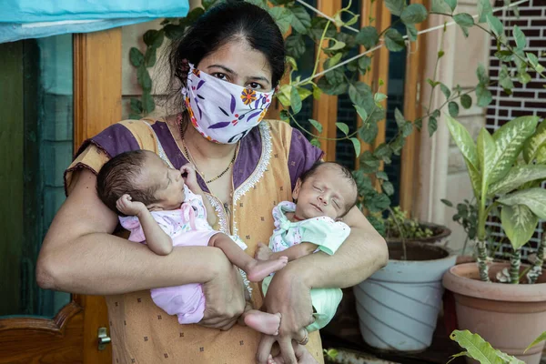 Young Mother Wearing Mask Holding Her Two Newborn Twin Babies, Stay Home Taking Extra Care Due To Covid-19 Pandemic.