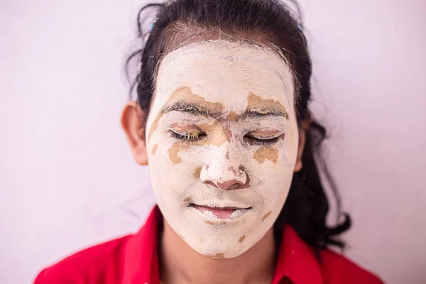 Young brunette girl with ayurvedic natural hearbal cosmetic facial mask applied over her face. multani mitti / fuller earth clay Pack against white background