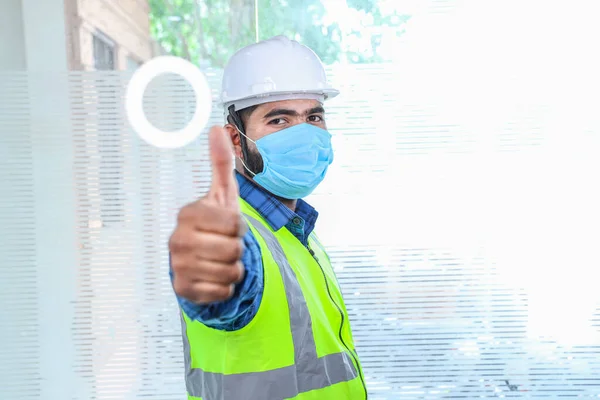 Maskeyi takan genç mühendis el hareketini onaylıyor ifadeyi onaylıyor sarı yelek ve beyaz kasklı mavi gömlekli adam tecrit bittikten sonra işe dönüyor.