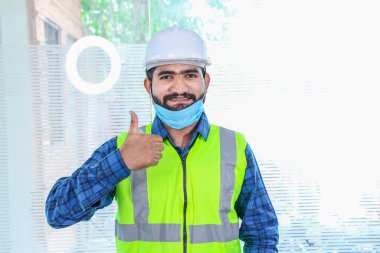 Maskeyi takan genç mühendis el hareketini onaylıyor ifadeyi onaylıyor sarı yelek ve beyaz kasklı mavi gömlekli adam tecrit bittikten sonra işe dönüyor.
