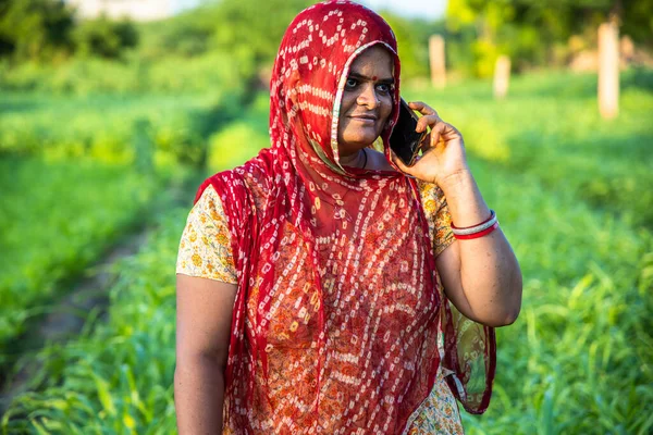 Traditional village women talking on mobile phone standing in green field agriculture land, happy indian female talking on phone.