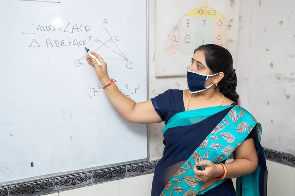 Maske takan kadın öğretmen ve sari sınıftaki beyaz tahtada matematik öğretiyor, Hindistan 'da okul eğitimi sınıfında covid19 salgını sırasında, yeni normal