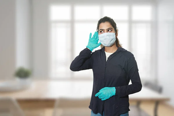 Young indian girl with surgical mask doing listening or hearing gesture wearing gloves and casual clothes, Copy space.