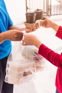 Mavi üniformalı Asyalı genç teslimatçı market servisi yapıyor. Kadın müşterilere plastik torbalar veriyor. Pandemik koronavirüs altında evlerini alıyorlar.