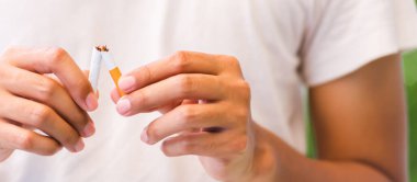 31 Mayıs Dünya Sigara Yok Günü, Asyalı sigara içen adam yeşil yapraklı arka planda sigara kırma, sigara içme veya bırakma kavramını kullanıyor.
