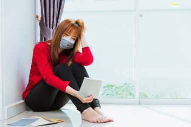 Asyalı üzgün kadın dizine sarılıp ağlıyor. Yüz maskesi takıyor. İşsiz karantinası, Coronavirus hastalığı ya da COVID-19.