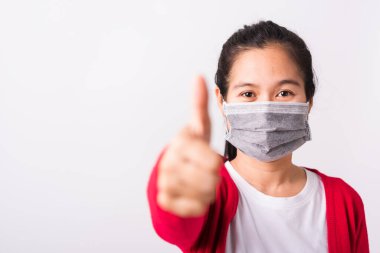 Koronavirüs veya COVID-19 virüsü veya filtre tozu veya hava kirliliğinden korunan kırmızı tişört ve yüz maskesi takan Asyalı yetişkin kadın parmağını iyiye işaret için kaldırıyor, beyaz arka plan izole edilmiş.