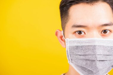 Yüzüne koruyucu mikrop veya hava tozu takan Asyalı genç adam, sarı arka plan ve fotokopi alanında izole edilmiş stüdyo çekimi, tıbbi salgın Coronavirus COVID-19 konsepti