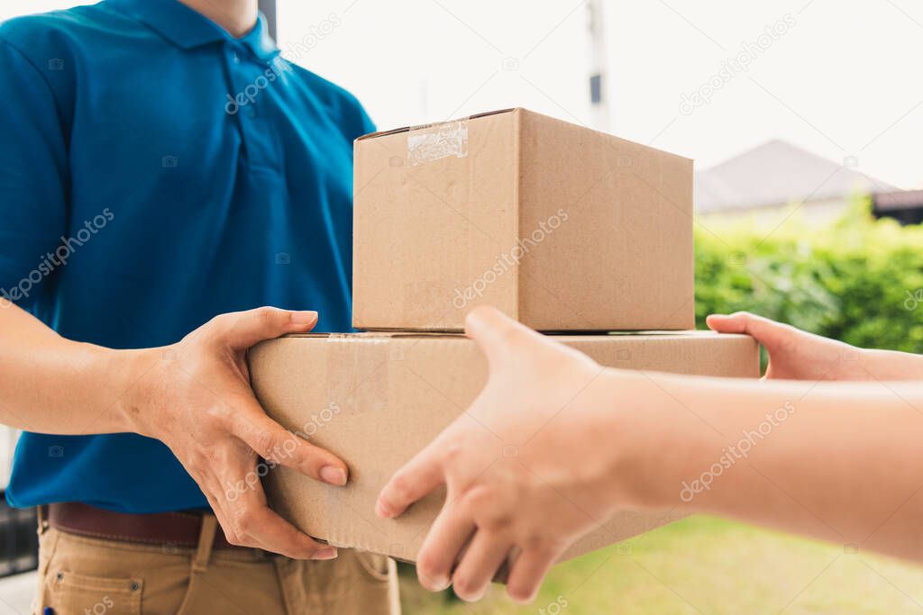 Asian delivery express courier young man giving boxes to woman customer receiving both protective face mask, under curfew quarantine pandemic coronavirus COVID-19