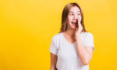 Asya Taylandlı mutlu bir portre güzel bir kadın tişört giyer dudaklarına el ele tutuşur gizli dedikodular fısıldar izole edilmiş fotoğraf stüdyosuna bakar sarı arka planda fotokopi çekilir