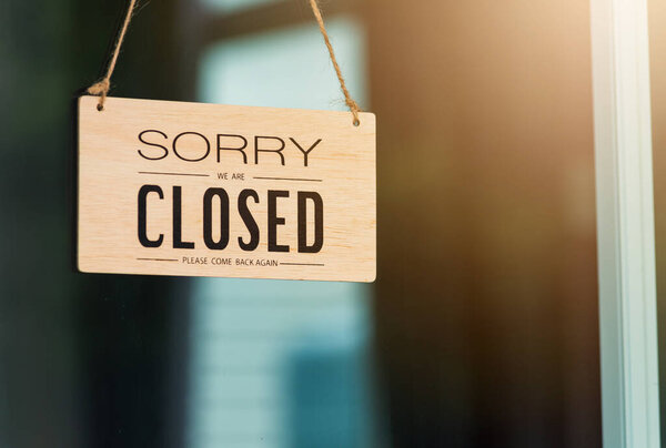 Close up of SORRY WE ARE CLOSED PLEASE COME BACK AGAIN notice sign wood board label hanging through glass door front shop, Business close during coronavirus disease concept