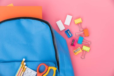 Mavi okul çantasının en üst düzlükte yatışı ve çocuk eğitimi için aksesuar araçları pembe arka planda, okula dönüş kavramı ve kullanım için fotokopi alanı