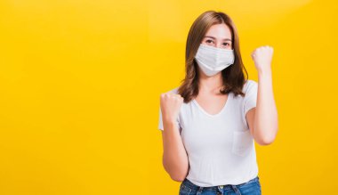 Yüz maskesi takan Asyalı güzel genç kadın toz filtresi pm2.5, COVID virüsü ve hava kirliliği sarı arka planda hastalıktan kurtulduktan sonra sevinçten havalara uçtu.