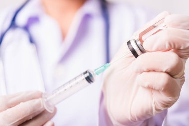 Kadın doktor, hemşire ya da üniformalı bilim adamı laboratuvar ortamında maske takıyor. Aşı şişesine şırınga enjekte ediyor. Tıbbi salgın Coronavirus COVID-19 kavramı.