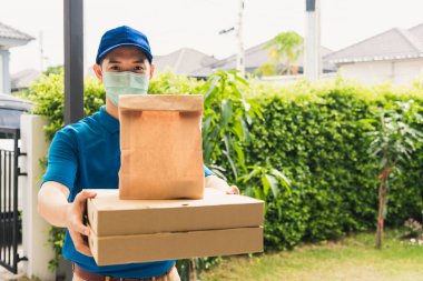 Asya 'lı genç kurye, üniformalı fast food pizzası gönderip tutuyor. Sokağa çıkma yasağı olan karantina altındaki yüz maskeli müşteri COVID-19' da koruyucu yüz maskesi kullanıyor.