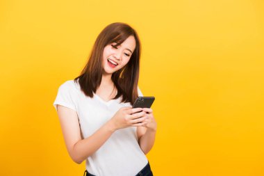 Asya mutlu portresi güzel, genç bir kadın gülümsüyor oyun oynuyor ya da akıllı telefondan mesaj yazıyor izole edilmiş telefona bakıyor, sarı arka planda fotokopi alanı olan stüdyoya bakıyor.